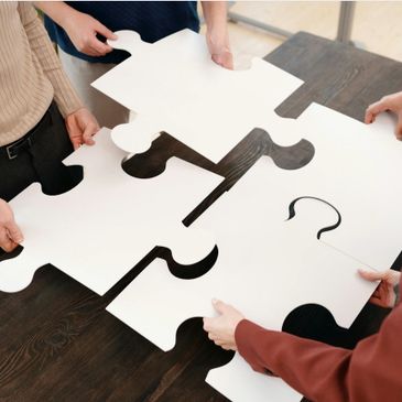 Four people assembling large white puzzle pieces with question marks on a table.