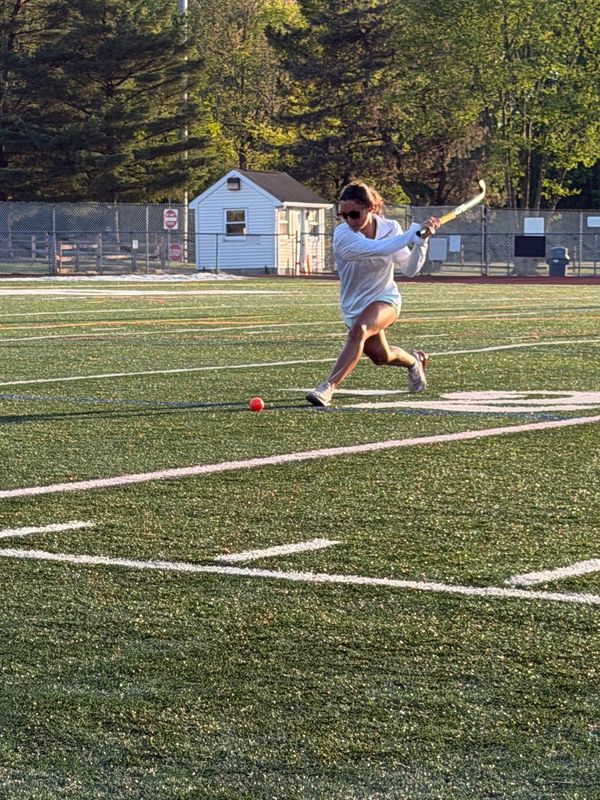 Player in white hitting a ball on a sports field.