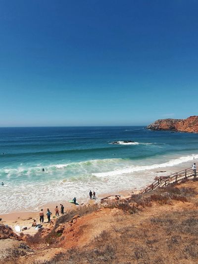 Rocky beach with aqua ocean and blue skies with some people walking on the beach