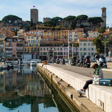 Woman sitting along pier in front of hillside village of colored houses
