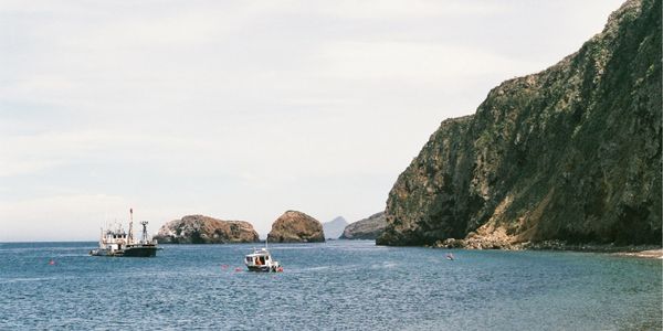 Two boats in ocean next to cliffs coming down into the ocean
