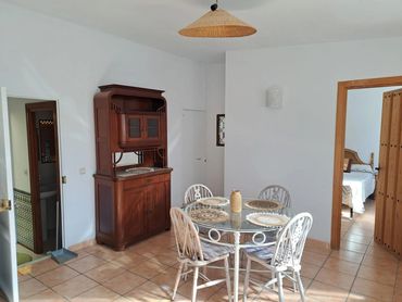 Sunlit dining area with a glass table, wicker chairs, and wooden cabinet in a cozy home.