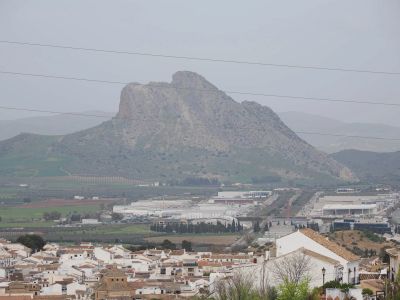 A mountainous landscape with a town and industrial area in the foreground under a cloudy sky.