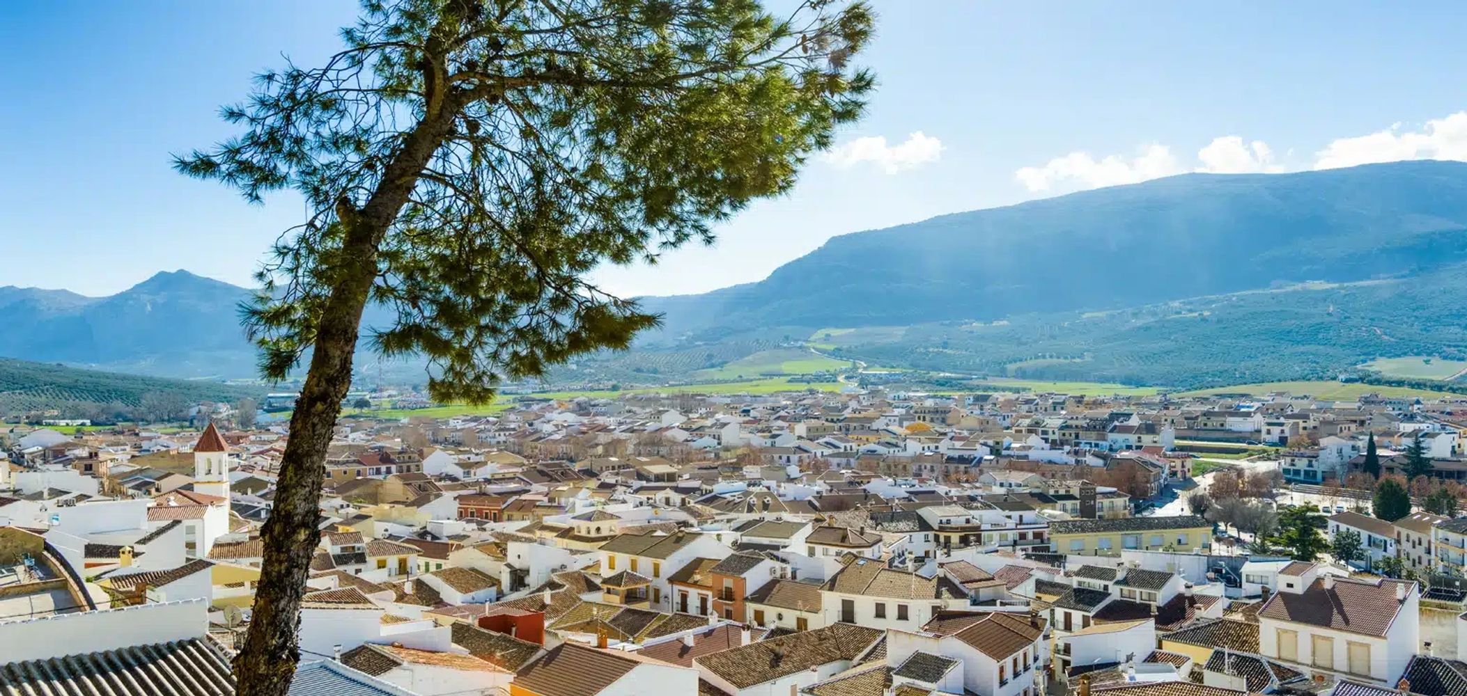 Scenic view of a town with tiled roofs and surrounding mountains under a clear blue sky.