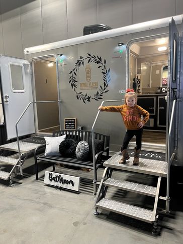 young girl posing in front of a portable restroom trailer with the interior in view