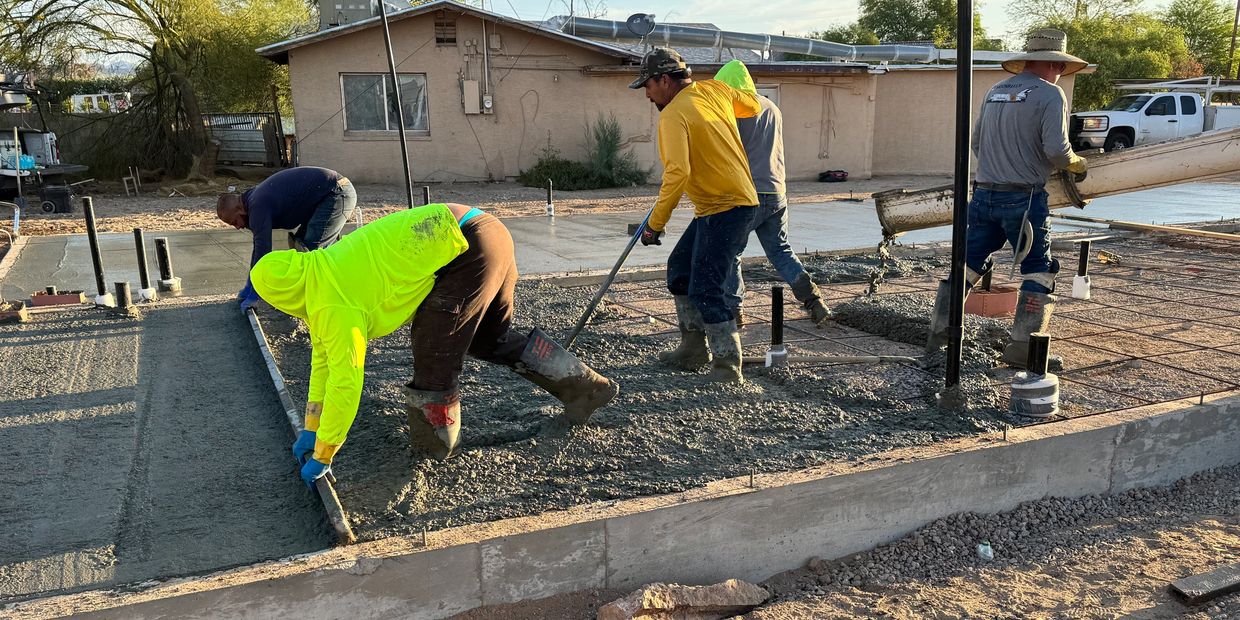 Workers pouring and smoothing concrete at a construction site.