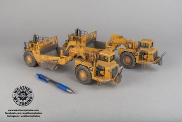 Two detailed yellow scale model construction vehicles next to a pen for size comparison.