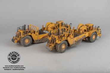Two detailed yellow weathering model trains on a gray surface.