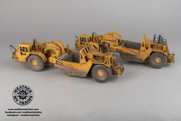 Three detailed yellow construction vehicle models on a gray surface.