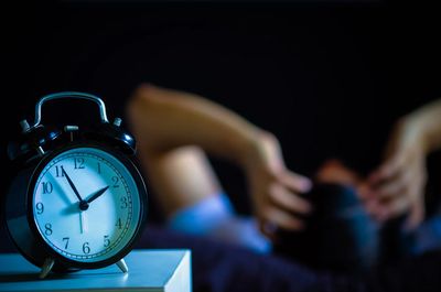 Black alarm clock showing 12:55 with a person blurred in the background.