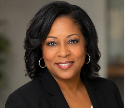 Professional woman smiling in a black blazer with hoop earrings.