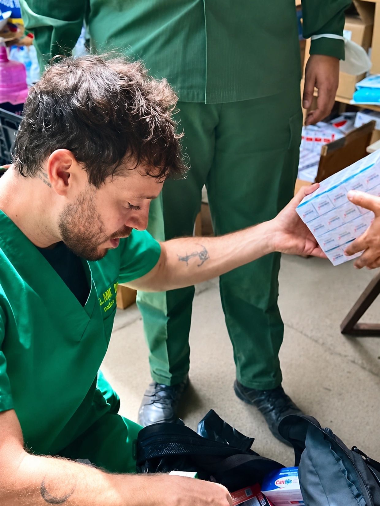 Man in green scrubs handling medical supplies.