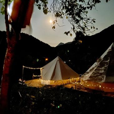 Tents illuminated by string lights under a starry night sky in a mountainous area.