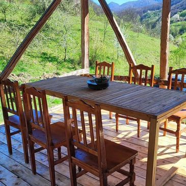 Wooden table and chairs set on a porch with scenic green hills.
