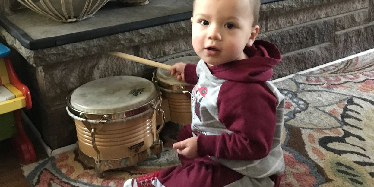 A toddler playing drums with a drumstick indoors.