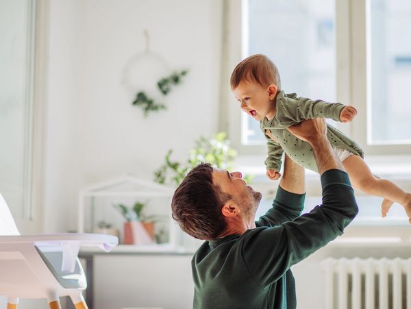 Father carrying baby son and they playing around in living room