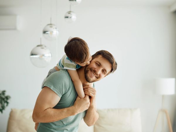 Little boy kissing his father who is piggybacking him while spending time together at home.