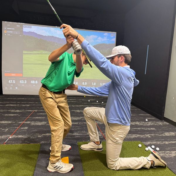Golf instructor guiding a young player indoors with swing analysis.