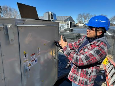 Technician in blue helmet inspecting rooftop HVAC unit.