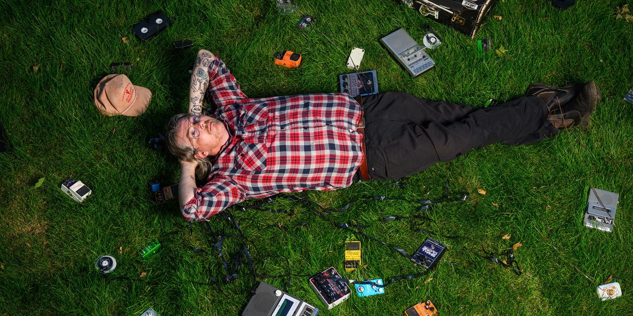 alexjcurrie lying ghe grass surrounded by guitar pedals and magnetic tape.