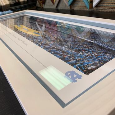 Framed photo of a packed basketball arena with North Carolina branding.