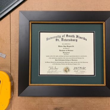 Framed University of South Florida diploma on a wooden surface with a tape dispenser.
