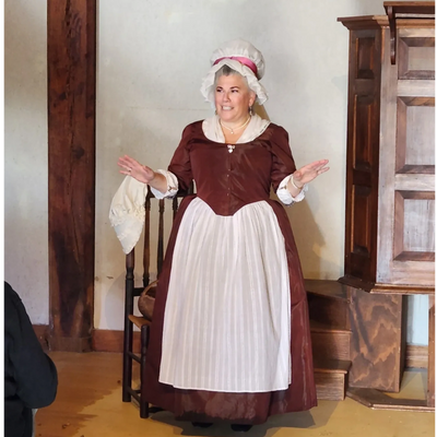 Martha Washington, in a brown silk round gown, entertains her guests with stories about her life.