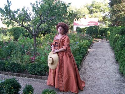 Sandy Spector strolls the Upper Garden in an orange silk sacque gown at Mount Vernon.