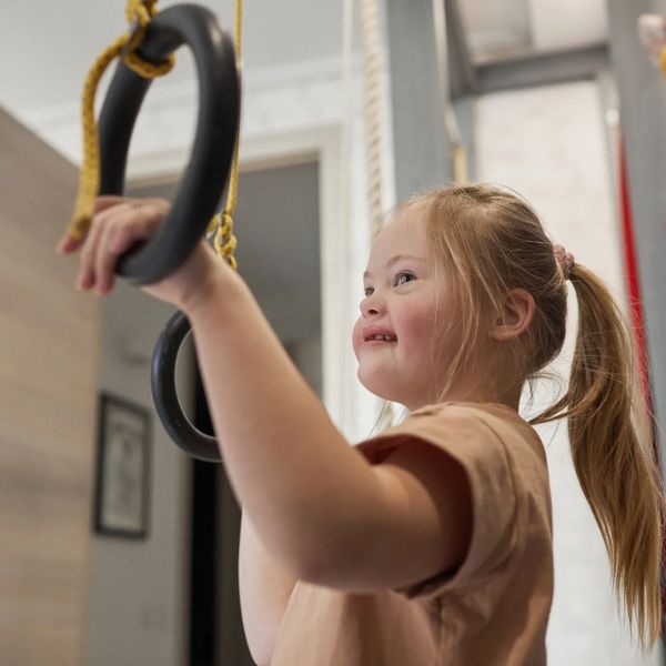 Young girl with Down syndrome playing on gymnastic rings indoors.