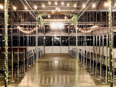 An aisle with chairs on both sides decorated with hanging greenery and string lights.