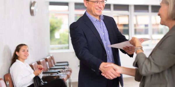 Man shaking hands with woman while another woman applauds in a waiting area.