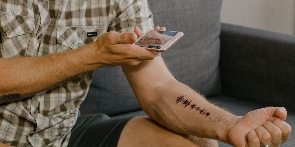 Man comparing tattoo on arm with soundwave image on phone.