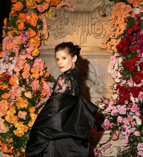 Woman in black dress poses among colorful flowers.