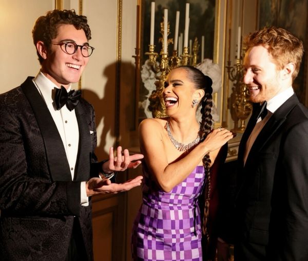 Three people dressed formally, laughing and chatting indoors.