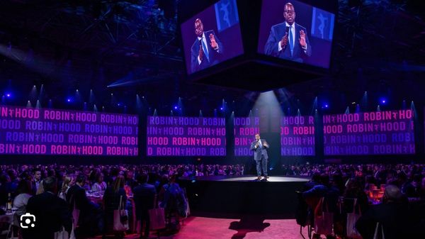 Speaker addresses audience at Robin Hood event with large screens.