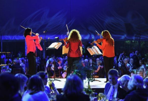 Trio of violinists playing in front of an audience at a formal event.