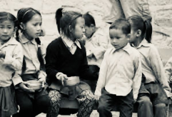Children sitting and standing, holding bowls.
