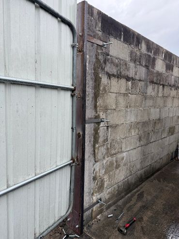 Concrete block wall with metal gate and scattered tools on wet ground.