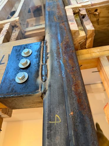 Close-up of a metal beam with bolts and wooden framing in construction.