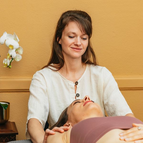 Woman standing providing shoulder massage to another woman laying down.