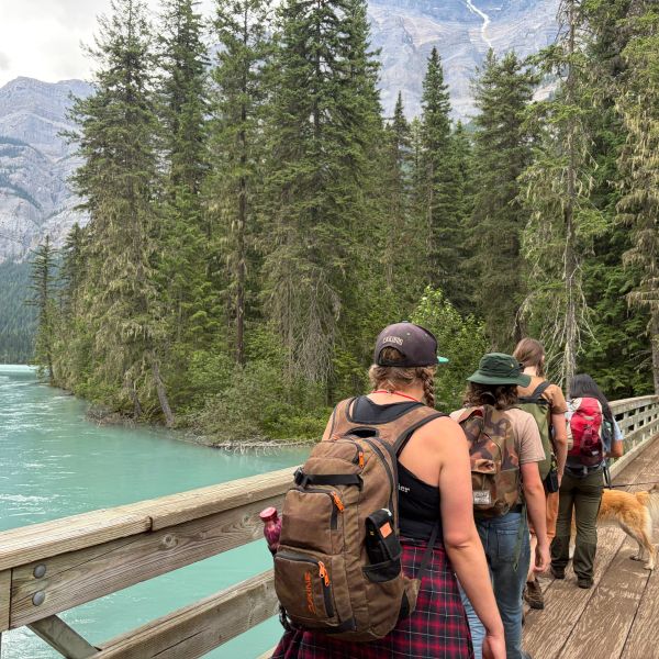 Group hiking near a turquoise river and pine trees.