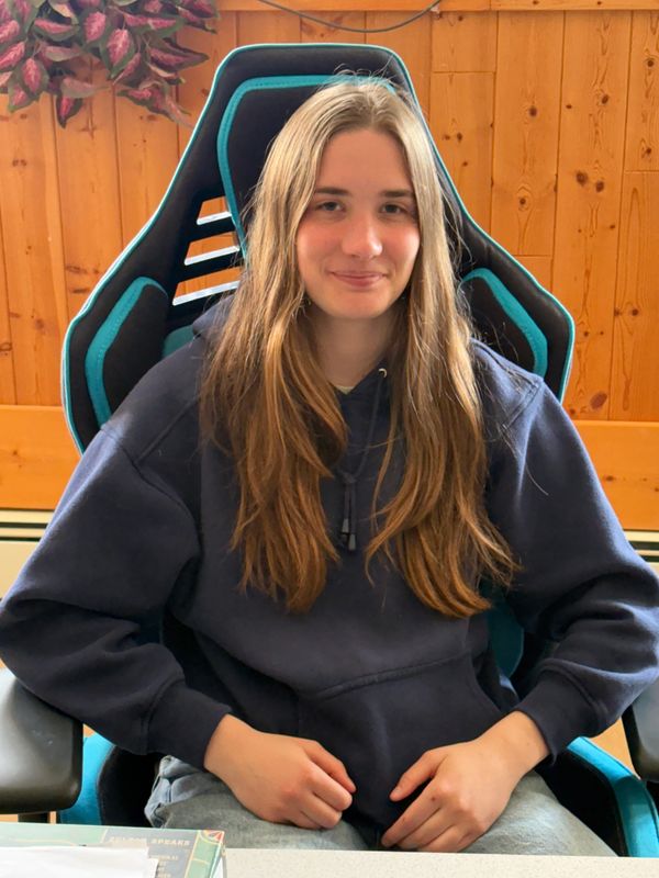 Young woman with long brown hair sitting in a gaming chair indoors.