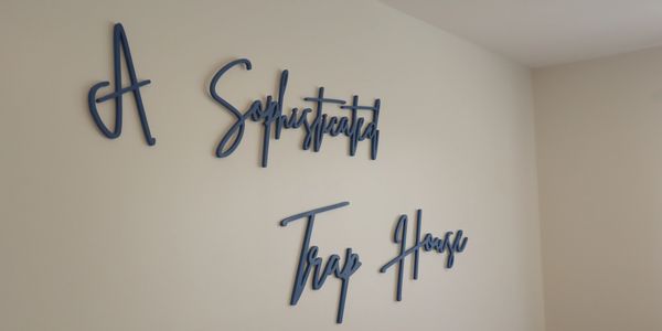 Blue cursive wall art saying 'A Sophisticated Trap House' in a cozy room.