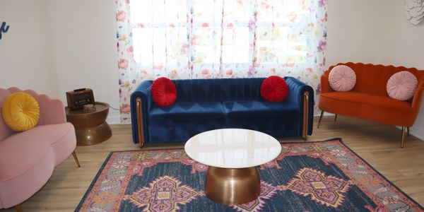 Colorful living room with velvet sofas, round pillows, floral curtains, and a patterned rug.