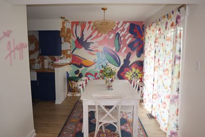 Bright dining room with floral mural, white wooden table, and floral curtains.