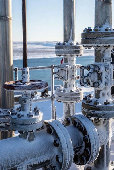 Frozen industrial pipes and valves covered in snow in a cold outdoor setting.