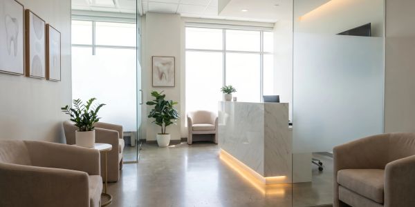 Modern dental office waiting area with beige chairs and plants.