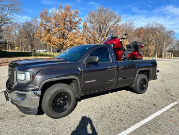 Black GMC Sierra truck carrying a red motorcycle in its bed on a sunny day.