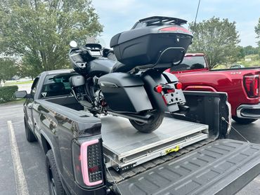 Black motorcycle loaded on a black pickup truck bed in a parking lot.