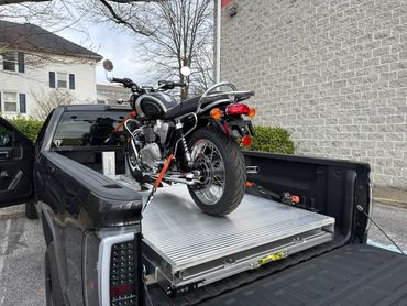 Classic motorcycle secured in the bed of a black pickup truck.